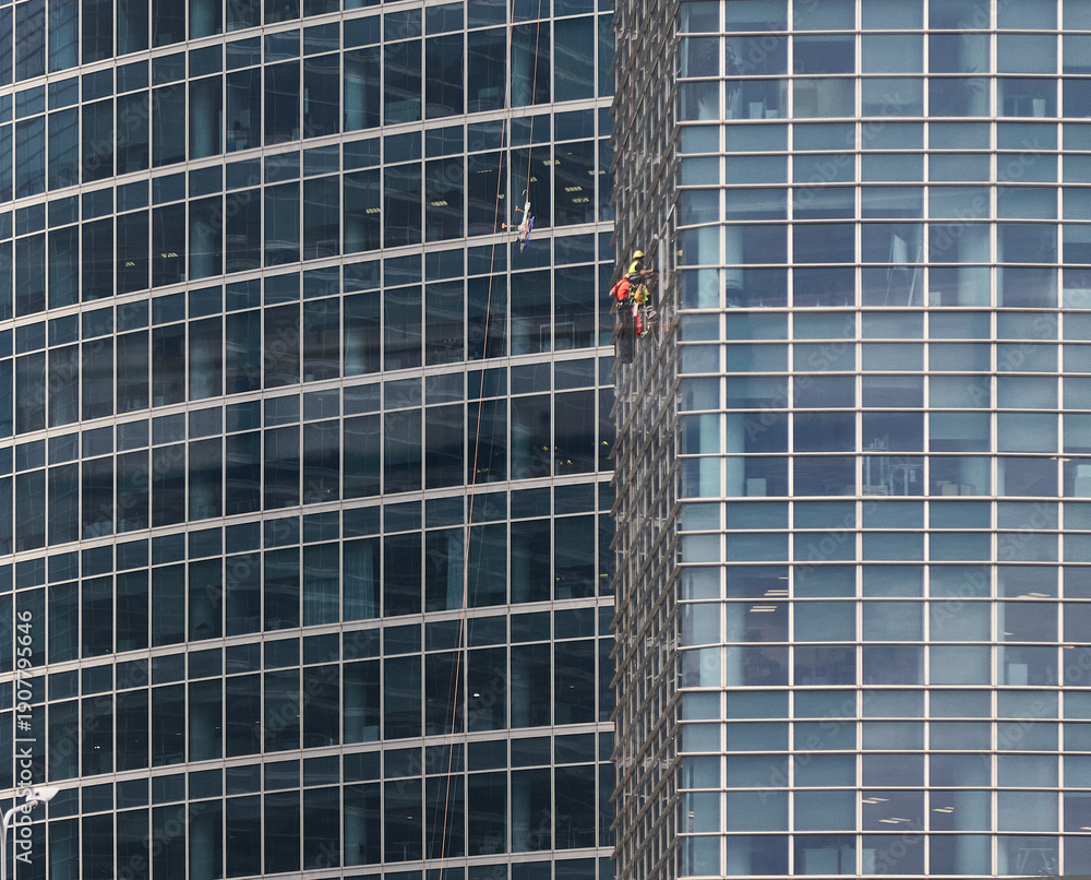 Obraz premium Window washers cleaning the glass facade of a modern skyscraper with reflective surfaces and geometric patterns in an urban setting