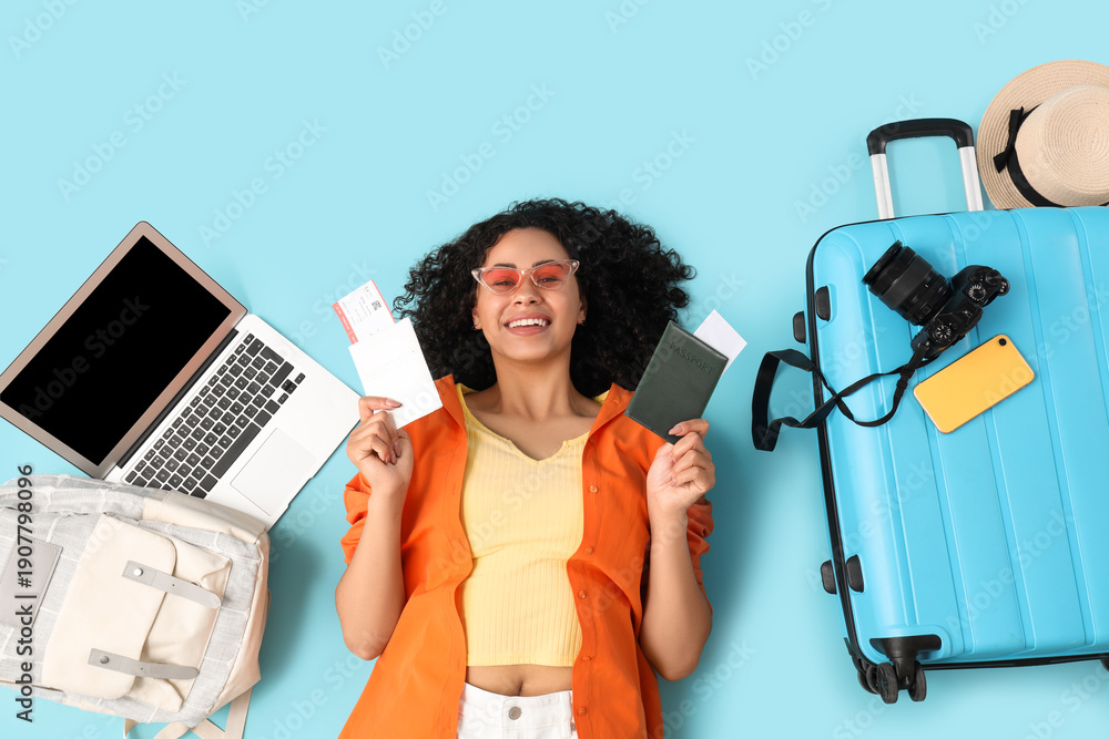 Naklejka premium Young female African-American tourist with passport, tickets, laptop and travelling accessories lying on blue background