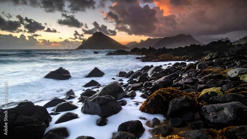 A coastal scene at dusk features mountains, rocks, waves, and a dramatic cloudy sky