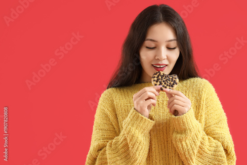 Young Asian woman eating cookie on red background