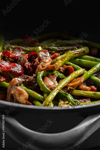 Asparagus, bacon and sliced mushroom fried in a ceramic frying pan background backdrop. Cooking seasonal vegetable concept.