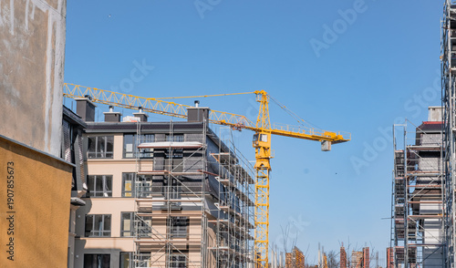 Apartment block under construction with a large yellow crane. Building site with scaffolding for urban development and real estate.