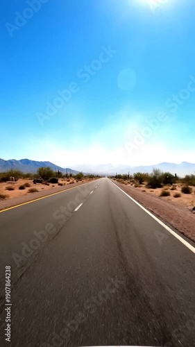Long desert highway stretches towards distant mountains under a clear blue sky.