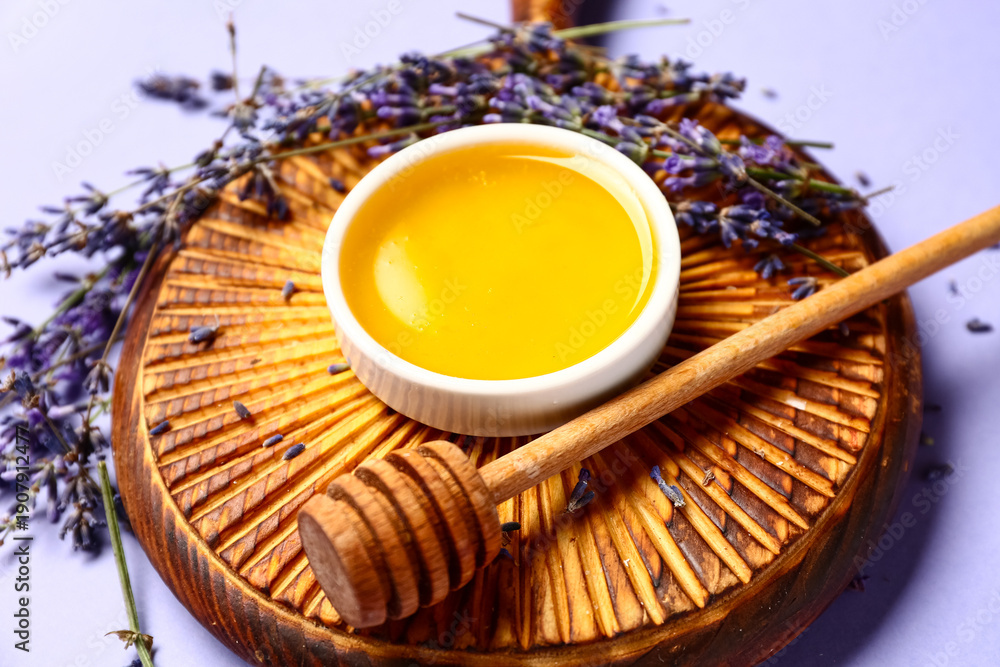 Obraz premium Wooden board with bowl of sweet lavender honey, dipper and flowers on blue background