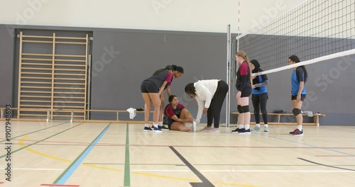 Ankle pain causing Indian athlete clutching ankle while coach inspecting, teammates rushing in gym