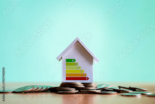 A model house with an energy efficiency meter based on a stack of coins; a concept for saving energy in homes, sustainable real estate investment, and eco-friendly housing.
