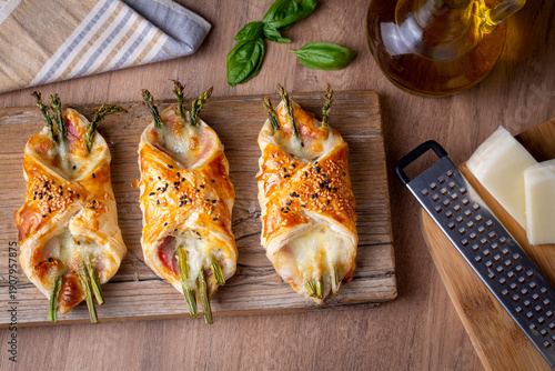 Baked green asparagus with ham and cheese in puff pastry sprinkled with sesame seeds and green basil leaves.