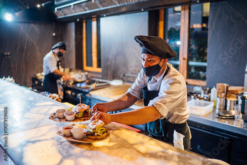 Chef wearing protective face mask preparing burgers in restaurant kitchen