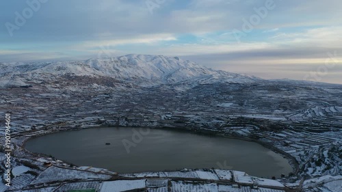 Aerial view of Lake Ram at a winter sunrise in the Golan Heights with the snowy Mount Hermon and Majdal Shams in the background