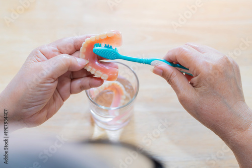 Photography Rear view of an elderly person holds a full upper denture while cleaning it with