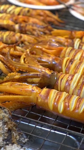 Grilling squid at a night market in the city with friends enjoying fresh seafood snacks. Traditional Thai street food