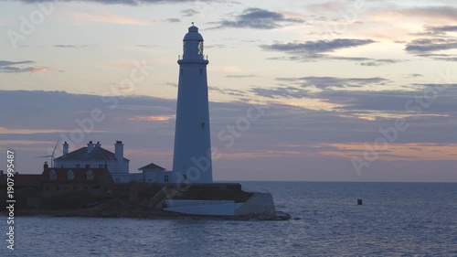 A static medium shot of the historic St Mary’s Lighthouse in Whitley Bay during a winter dawn. The white tower and red-roofed cottages sit on a tidal island