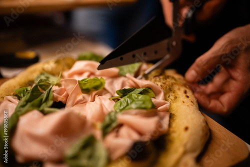 Fotografija Chef cutting pinsa romana with mortadella basil