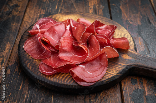 Foto Thin cured beef slices bresaola meat arranged on a rustic wooden board with fresh rosemary over a dark textured background