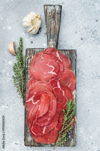 Foto Lean cured beef Cecina arranged neatly with herbs on a wooden board, showcasing vibrant red color over a minimal grey stone background