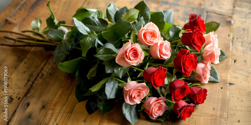 Bouquet of pink and red roses arranged with green leaves on a rustic wooden table, showcasing vibrant colors and natural beauty in a floral display