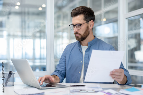 Quadro su tela Confident businessman wearing glasses and a casual shirt working on his laptop,