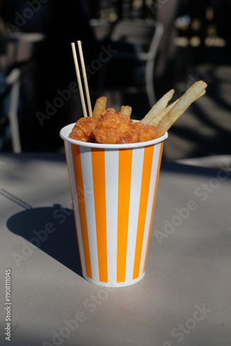 French fries and fried chicken served in a paper cup at a food truck
