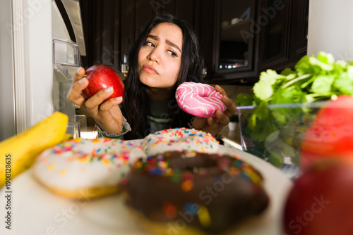 Konstfotografi Woman weighing a healthy apple against an unhealthy donut inside a refrigerator,