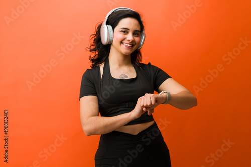 Active woman smiling and checking fitness tracker during studio workout, listening to music with headphones