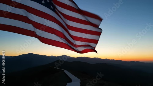 Wallpaper Mural Majestic american flag waving gently in the breeze on a mountain summit, with a beautiful sunset creating a vibrant orange glow on the horizon behind the silhouetted peaks of a mountain range Torontodigital.ca