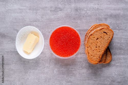 Red caviar, butter, and slices of rye bread. Ingredients for making sandwich on gray table. Top view