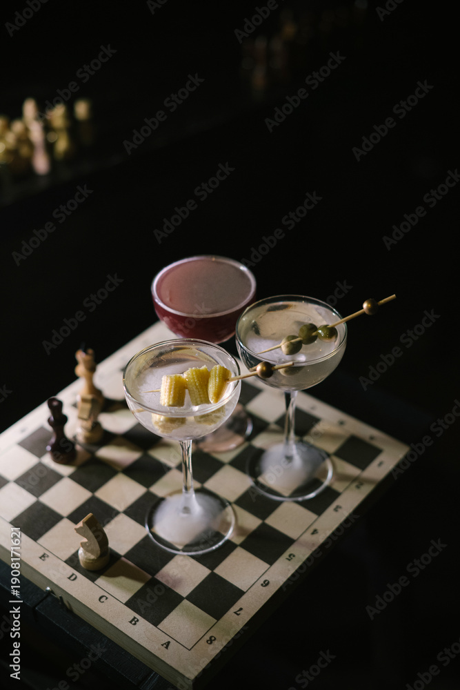 custom made wallpaper toronto digitalThree Martini cocktails, two differently garnished dirty martinis and a twist on espresso martini, standing on a wooden chess board in the dark room, close up view