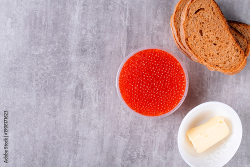 Red caviar, butter, and slices of rye bread. Ingredients for making sandwich on gray table. Top view, copy space