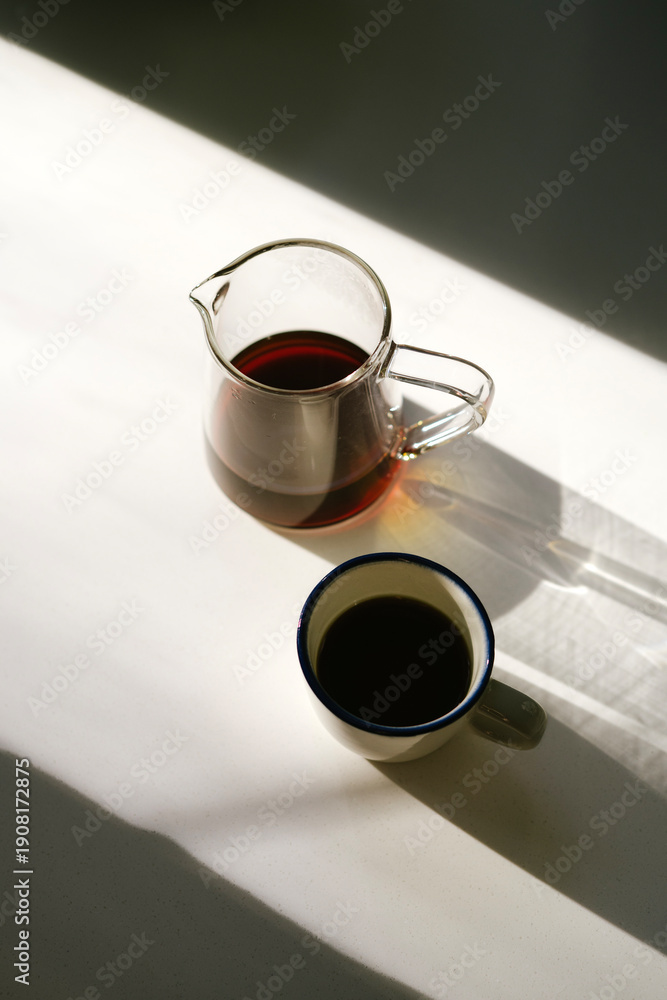 custom made wallpaper toronto digitalA cup of freshly brewed hot black filter coffee and a server full of it, standing on the white surface in the sun, making soft golden shades, top view, flat lay, vertical image 