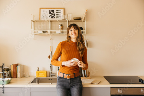 Billede på lærred Woman smiling holding coffee mug in modern kitchen