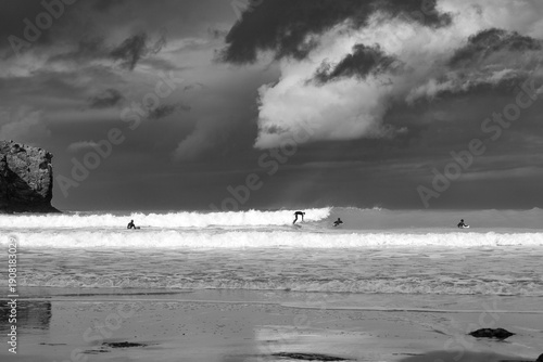 Canvas Print Black and White photo of surfers surfing waves under stormy skies in Cornwall