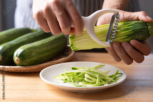 Hands using julienne peeler to slice green zucchini into noodles (zoodles), preparing healthy food