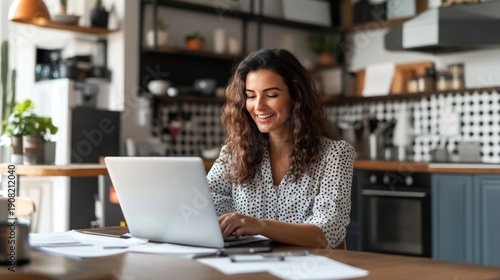 Happy woman sitting at the kitchen table with a laptop, checking documents and reviewing bills, staying organized