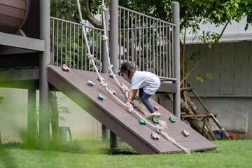 Young child climbing playground structure with rope, outdoor activity for learning and development. Concept of growth, confidence, childhood education, effort, challenge and active play.