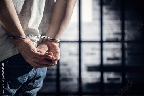 Arrested criminal wearing handcuffs with handcuffed hands behind back in prison