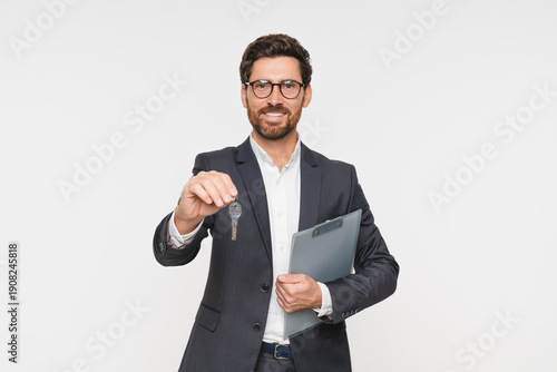 Real estate agent realtor lawyer wearing smart casual suit and glasses holding key from new apartment and clipboard contract on white background. Banker seller owner tenant ready to move in concept