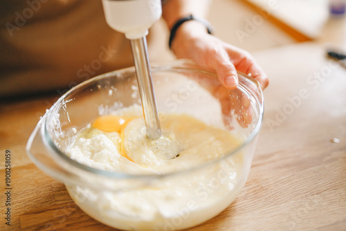 Mixing ingredients in a glass bowl with an electric blender at a kitchen countertop in the afternoon
