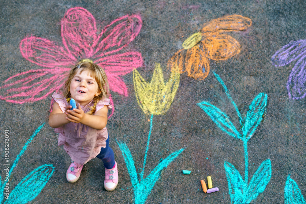 Obraz premium Toddler girl drawing colorful flowers with sidewalk chalk outdoors, top view of creative play on pavement showing carefree childhood, real people