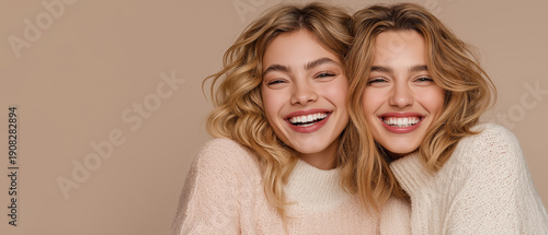 Two happy women hugging smiling portrait on beige background