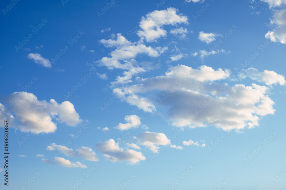 Fototapeta premium Bright blue sky with scattered white soft clouds on a sunny day, creating a calm and airy natural background for design use.