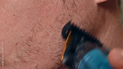 A young man or teenager shaves with an electric trimmer. Close-up. Men's personal hygiene.