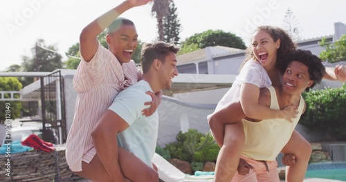 Two happy diverse male friends holding piggyback female friends in backyard at pool party