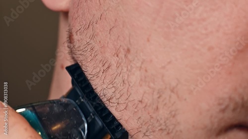 A young man or teenager shaves with an electric trimmer. Close-up. Men's personal hygiene.