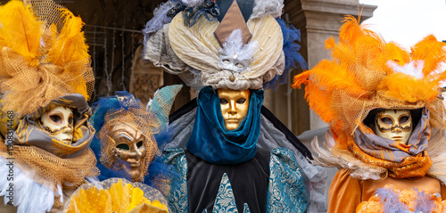 Fototapeta Three performers in elaborate Venetian carnival costumes pose under historic arc