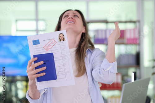 Obraz na płótnie A young woman stands in a well-lit office, holding a rejected visa application and a passport