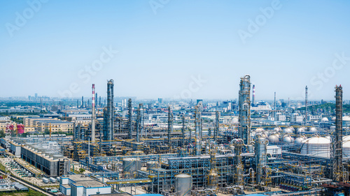 Industrial chemical plant with complex steel pipelines and storage tanks under a clear blue sky.