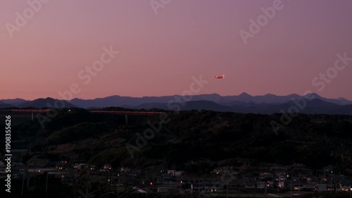 夕暮れの空を着陸するジェット機と遠くの山並み、誘導灯が輝く日本の風景
