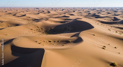 Breathtaking aerial view of rolling sand dunes in a vast desert landscape under a clear sky, featuring intricate wind patterns.
