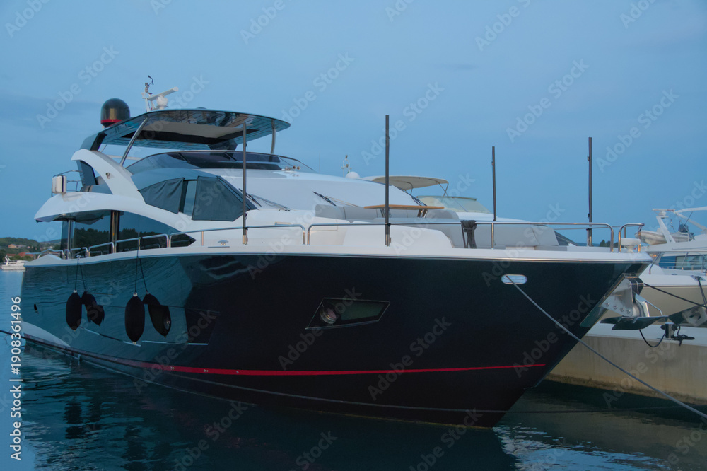Fototapeta premium Large luxury motor yacht with dark hull and red stripe moored