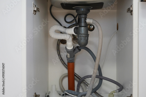 Under sink plumbing pipes and drainage system inside kitchen cabinet
